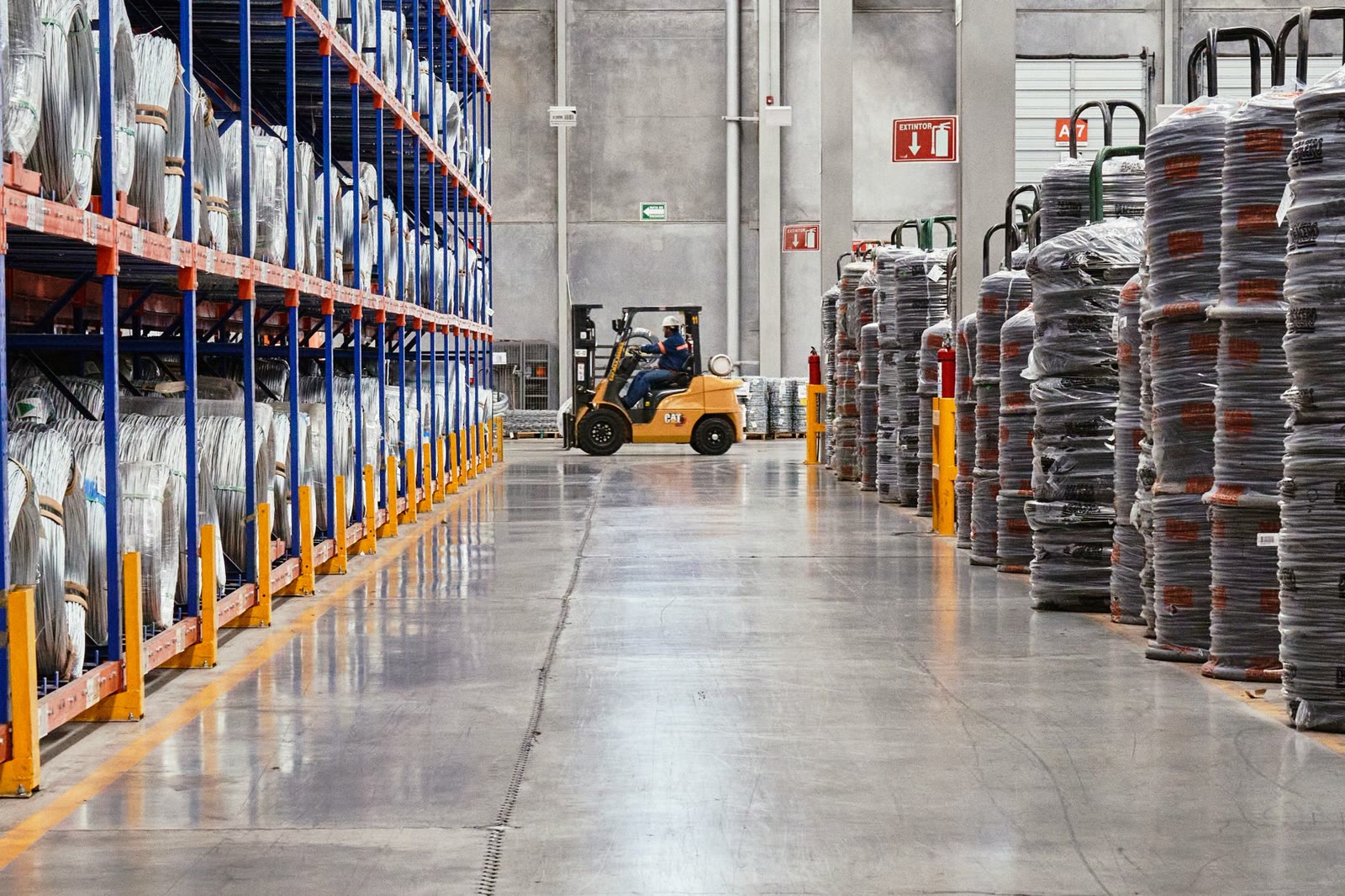 A forklift moving stacked goods down a warehouse aisle